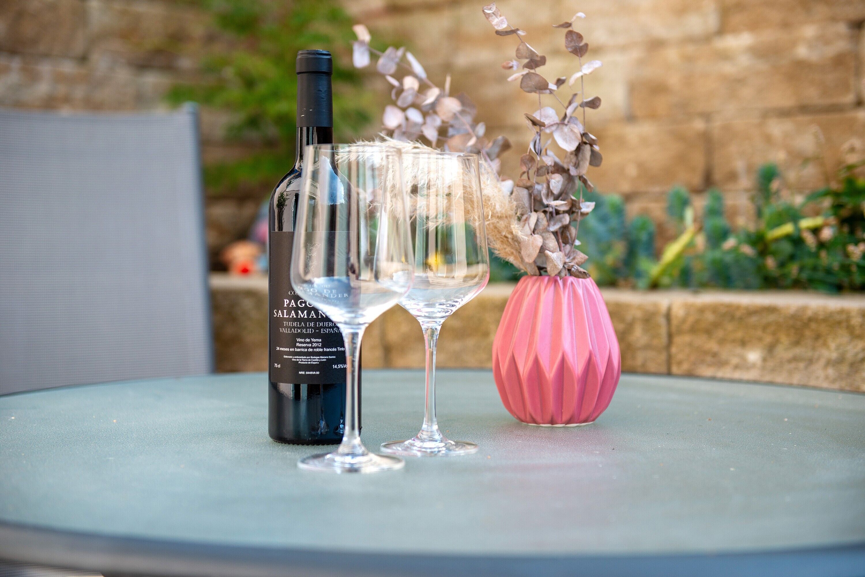 A bottle of wine, two glasses, and a pink vase on a table.