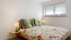 Ein Schlafzimmer mit einem Bett, zwei Nachttischlampen, einem Fenster mit Jalousien und einer Wanddekoration in Herzform.