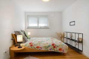 Een slaapkamer met een bed, bedlamp, raam en een zwart metalen rek.