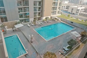 A rooftop swimming pool with lounge chairs and umbrellas, surrounded by modern buildings.