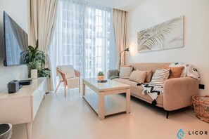A modern living room with a sofa, a coffee table, a desk with a computer, and a large window with curtains. - Inviting 2BR Apartment - Only 10 Mins to Downtown - Sobha Creek Vista Reserve (Dubai)