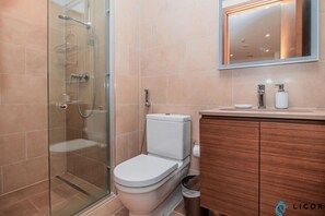 A modern bathroom with a glass shower enclosure, a white toilet, and a wooden vanity with a mirror above.