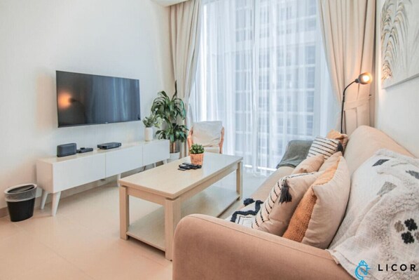 A modern living room with a flat-screen TV, a white cabinet, a wooden coffee table, and a beige sofa with patterned cushions.