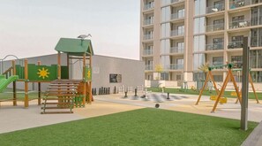 A playground with climbing structures, a slide, and a chess table in an urban setting. - Inviting 2BR Apartment - Only 10 Mins to Downtown - Sobha Creek Vista Reserve (Dubai)