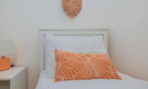 Un lit avec une tête de lit blanche et un coussin à motifs orange.
