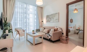 Un salon moderne avec un canapé, une table basse et un fauteuil. Il y a une grande fenêtre avec des rideaux, une plante fixée au mur et un miroir qui reflète la pièce.