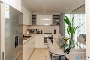 Een moderne keuken met witte kasten, een roestvrijstalen koelkast, een gasfornuis en een eethoek met een glazen tafel en stoelen.