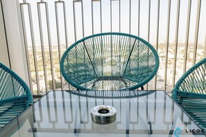 Un balcón con una mesa de vidrio y dos sillas de mimbre verde.
