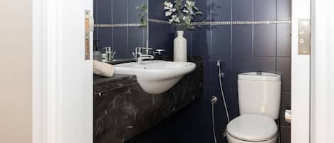 A modern bathroom with a white sink, dark marble countertop, and a white toilet.