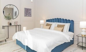 A neatly made bed with a blue headboard, white bedding, and decorative pillows. - Prime Spacious 2 BR Apt, Burj Khalifa & Canal View (Dubai)