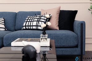 Un canapé bleu agrémenté de coussins à motifs noirs et blancs, d’un coussin beige et d’un coussin noir. Un vase en verre contenant des fleurs blanches et un objet noir sont posés sur une table devant le canapé.