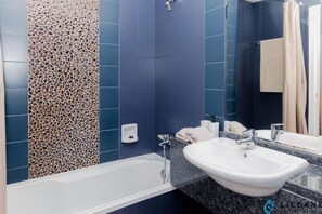 A modern bathroom with a white bathtub, a white sink, and a mirror. - Prime Spacious 2 BR Apt, Burj Khalifa & Canal View (Dubai)