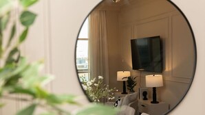 A hotel room with a large mirror reflecting a TV, two bedside lamps, a sofa, and a potted plant. - Prime Spacious 2 BR Apt, Burj Khalifa & Canal View (Dubai)