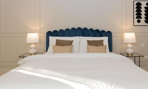 Un lit bien fait, avec une tête de lit rembourrée bleue, deux lampes de chevet et des coussins à motifs.