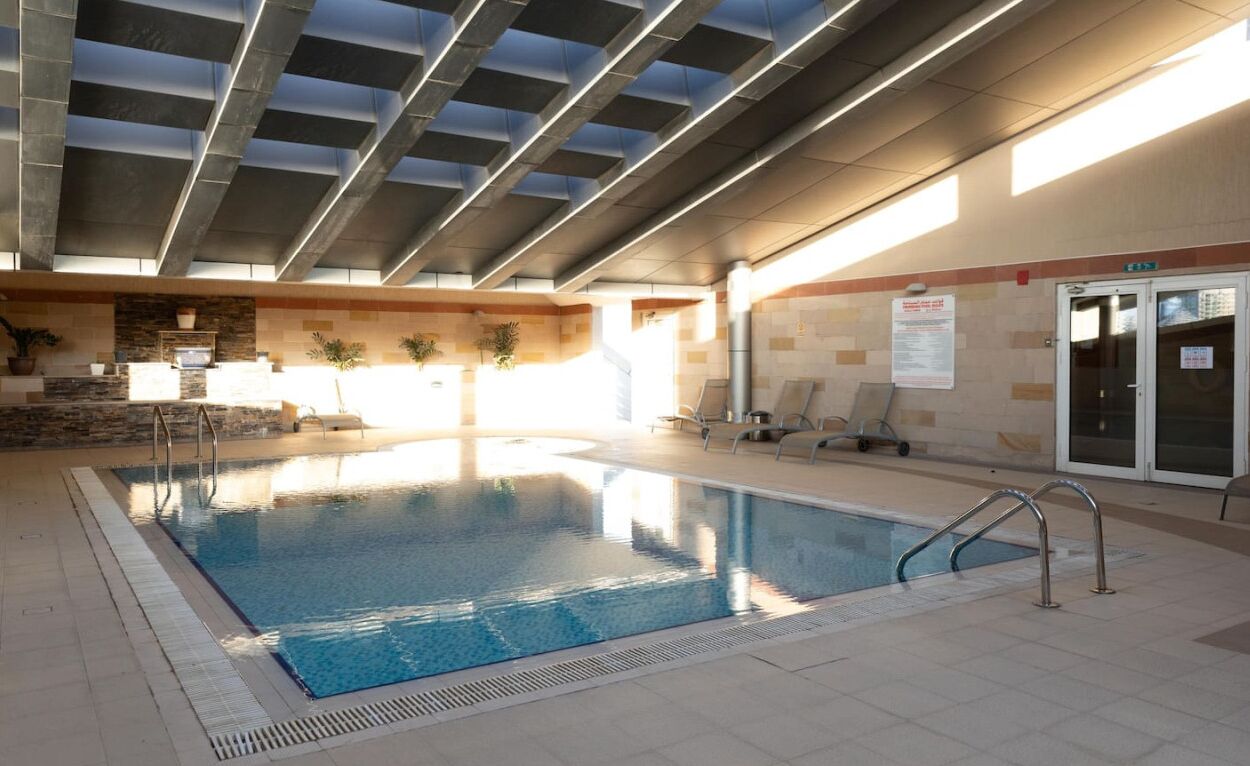 Una piscina interior con suelo de baldosas, techo con diseño de cuadrícula y pared con detalles de piedra.