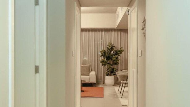 A hallway with a door on the left, a plant, a chair, and a table in the background. - Stylish 2BR Apt with pool view of Burj Khalifa - Downtown Views (Dubai)