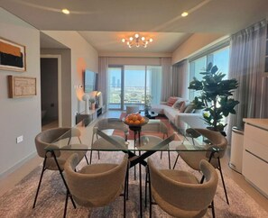 A modern living room with a glass dining table, comfortable seating, a large plant, and a view of the city.