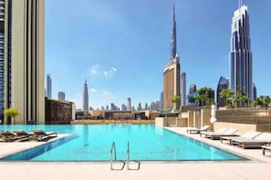 A swimming pool with lounge chairs, surrounded by high-rise buildings, including the Burj Khalifa.