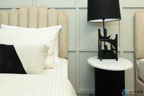 Una cama con almohadas blancas y negras, una mesita redonda con una lámpara negra y una pared con diseño de paneles.