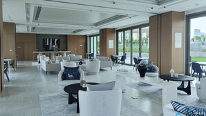 A modern hotel lobby with a spacious seating area, a reception desk, and large windows offering a view of the outdoors. - Stylish 2BR Apt with pool view of Burj Khalifa - Downtown Views (Dubai)