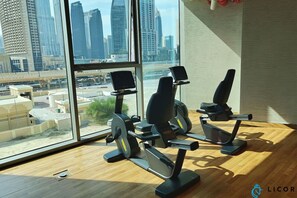 Un gimnasio con equipo de ejercicio y vistas a un paisaje urbano a través de amplias ventanas.