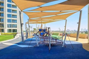 Un patio de juegos al aire libre con una estructura para escalar y una zona con sombra.
