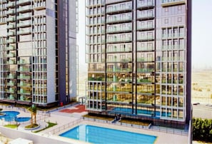 A high-rise residential building with multiple balconies, a swimming pool, and a landscaped area.