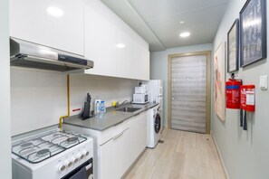 A compact kitchen with a gas stove, a microwave, a washing machine, and a sink. There are fire extinguishers on the wall and a door with a frosted glass panel.