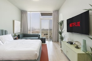 A modern hotel room with a large bed, a sofa, a TV mounted on the wall, and a view of the city through the window.