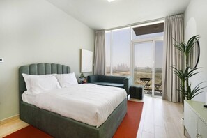 A bedroom with a large bed, a sofa, a balcony with a view, and a potted plant.