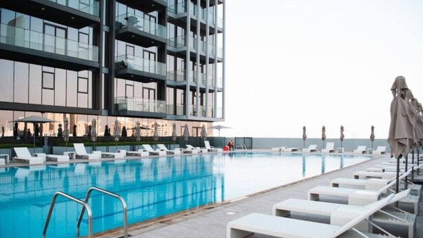 A modern hotel with a rooftop pool, lounge chairs, and a multi-story building with balconies. - Stylish Cozy Studio in Bloom Towers, Jumeirah Village Circle – Modern Comfort & City Views (Cosy Studio Apartment in Bloom Towers, Jumeirah Village Circle)