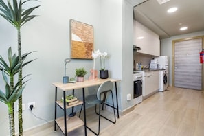 A compact kitchen with a washing machine, a coffee machine, and a small dining area with a table and chairs.