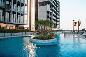 A modern building with a pool featuring a circular island with palm trees.