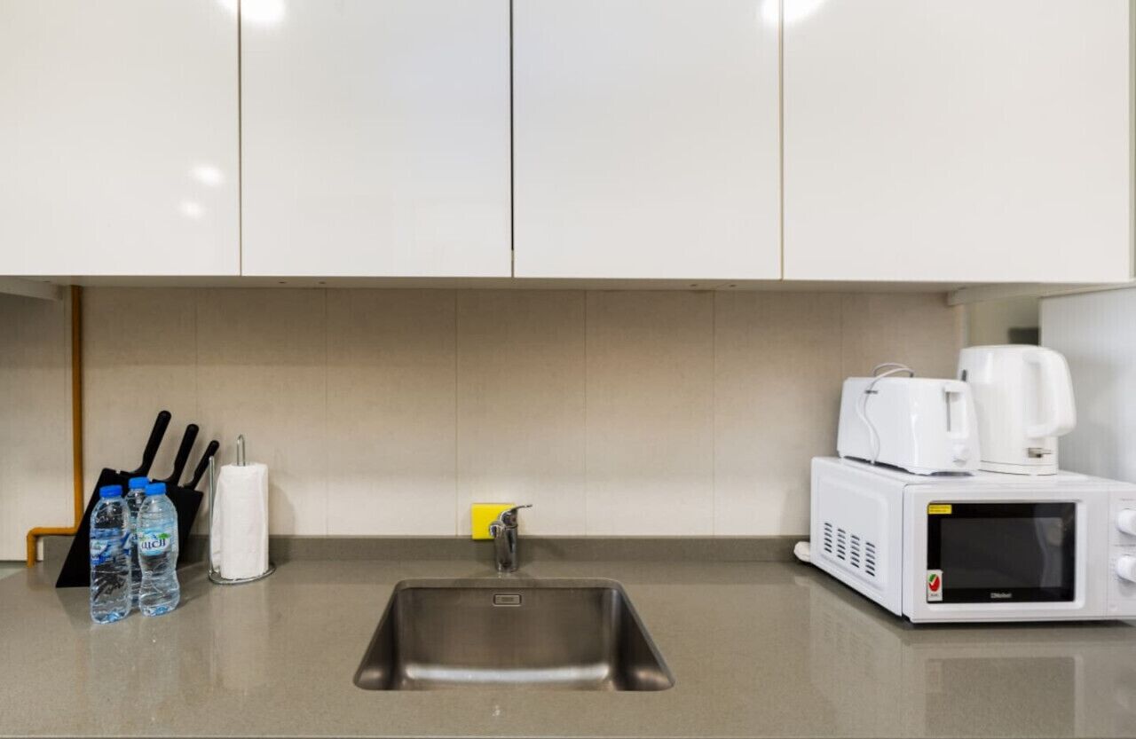 A kitchen with a stainless steel sink, a microwave, and a coffee maker. There are water bottles and a napkin holder on the counter.