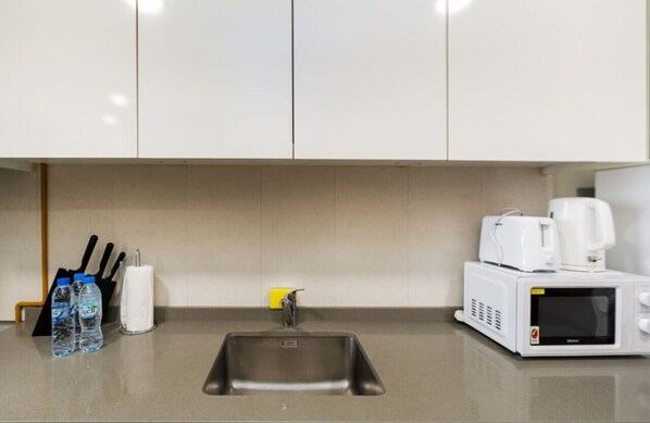 A kitchen with a stainless steel sink, a microwave, and a coffee maker. There are water bottles and a napkin holder on the counter.