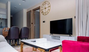 A modern living room with a flat-screen TV, a dining area with chairs, and a large wall clock.