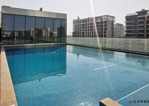 A rooftop swimming pool with clear blue water, surrounded by modern buildings. - Classic Elegance - 1BR with balcony in Sobha Waves (Dubai)