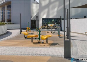 An outdoor fitness area with exercise equipment and benches. - Classic Elegance - 1BR with balcony in Sobha Waves (Dubai)