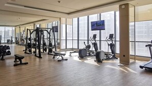 Una palestra con diverse attrezzature per esercizi, ampie finestre e uno schermo televisivo.