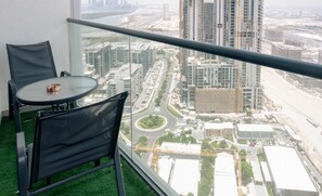 Uma varanda com mesa e cadeiras de vidro, com vista para um horizonte urbano com arranha-céus e uma estrada.