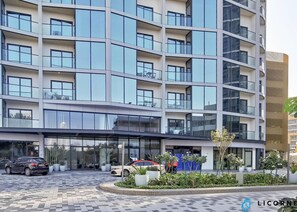 A modern multi-story hotel with a glass facade, outdoor seating area, and a landscaped garden.