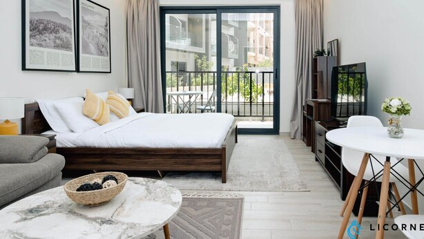 A modern bedroom with a bed, a small table, a sofa, a TV, and a balcony with a view of buildings. - Stylish Sanctuary Studio with Pool view (Dubai)