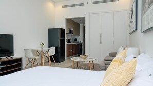 A modern hotel room with a large bed, a TV, a dining table with chairs, a kitchen area, and a sofa. - Stylish Sanctuary Studio with Pool view (Dubai)