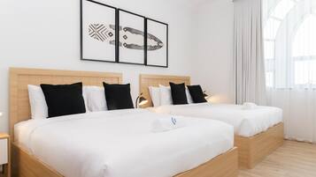 Une chambre d’hôtel avec deux lits, une tête de lit en bois, du linge de lit blanc et une grande fenêtre avec des rideaux.