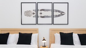 Una camera d'albergo con due letti, un comodino con una lampada e tre quadri appesi al muro.