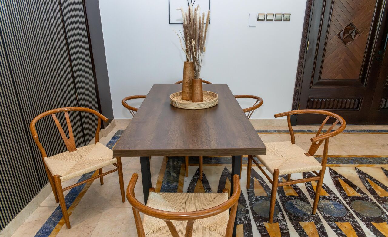 Een eettafel met een geweven decorstuk, omringd door vier houten stoelen met rieten zittingen.