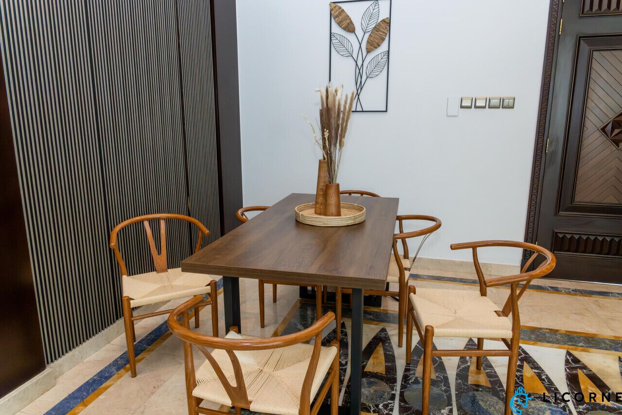 Ein Essbereich mit Holztisch und -stühlen, einer Vase mit Trockenpflanzen und einem an der Wand befestigten Lichtschalter.