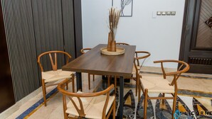 Zona pranzo con tavolo e sedie in legno, un vaso con piante essiccate e un interruttore della luce fissato al muro.