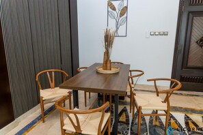 Een eethoek met een houten tafel en stoelen, een vaas met gedroogde planten en een lichtschakelaar aan de muur.