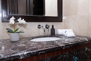 Un baño con lavamanos de mármol, un espejo, una orquídea en maceta y un perchero.